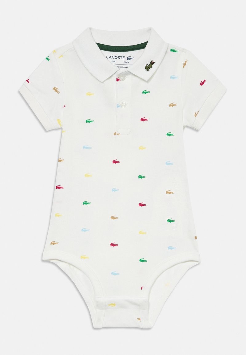Balts polo stila jumpsuit ar apkakli, kas rotāts ar košām Lacoste logo krāsās: sarkanā, zaļā, zilā, dzeltenā un brūnā. Izgatavots no mīksta kokvilnas auduma.