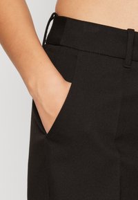 Černé tailored kalhoty s hladkou texturou, s boční kapsou a stahovací šňůrkou v pase.