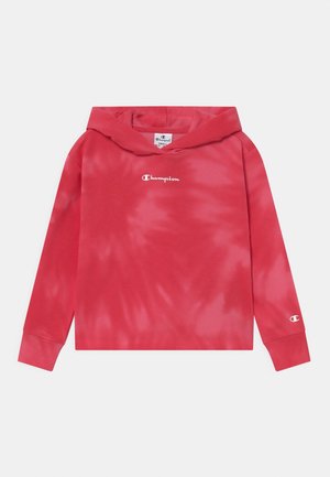 Sweat à capuche tie-dye rouge en matériau doux, avec une capuche à cordon et un petit logo blanc "Champion" sur la poitrine et la manche.