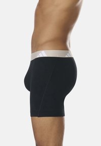 Boxers noirs avec une ceinture élastique beige portant un logo, conçus pour un ajustement serré, avec des coutures minimales, une texture lisse et une longueur moyenne.