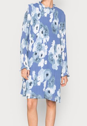 Blaues Langarmkleid mit großem weißem und grauem Blumenmuster, plissiertem Stoff und gerafftem Ausschnitt, getragen von einer stehenden Person.