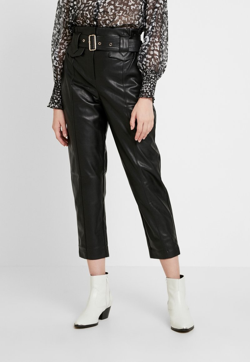 Svart läderbyxor med midja av bälte, kort längd och framfickor, kombinerat med en transparent mönstrad blus och vita ankelstövlar.