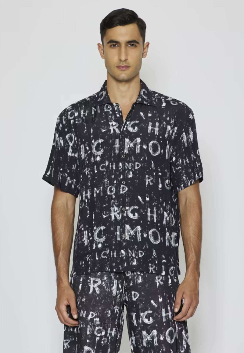 Camicia nera a maniche corte con un motivo di testo e grafiche bianche. Presenta un colletto e una chiusura con bottoni, realizzata in tessuto leggero.