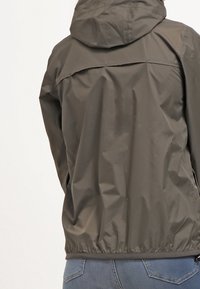 Ciemnooliwkowa wodoodporna kurtka z kapturem, elastycznym dołem i gładką fakturą. Posiada prosty design bez widocznych zapięć.