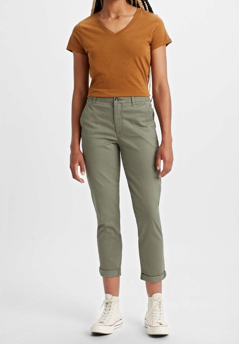Olivgrön, croppade byxor med upprullade cuffs, matchat med en kortärmad brun V-ringad t-shirt. Modellen bär vita högskor.