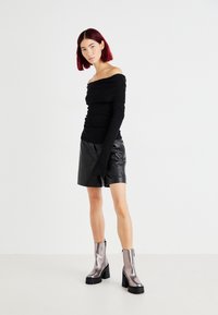 Top negro sin hombros con mangas largas, combinado con pantalones cortos de cuero negro y botas metálicas de tobillo con suelas gruesas. Diseño simple, sin patrones.