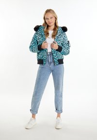 Giacca puffer con stampa leopardata teal, cappuccio con bordo in pelliccia, polsini a coste neri e chiusura con zip. Abbinata a jeans di denim blu chiaro a vita alta.