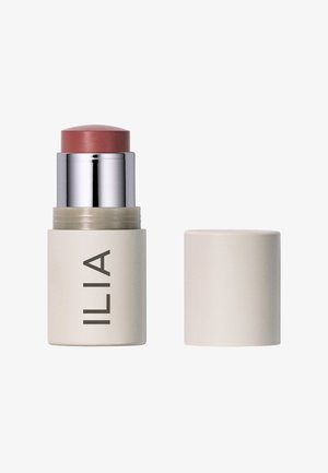 ILIA cream blush stick in een matte beige verpakking met zilveren accenten. De bovenkant heeft een afgeronde, perzikkleurige product. De dop zit aan de zijkant.
