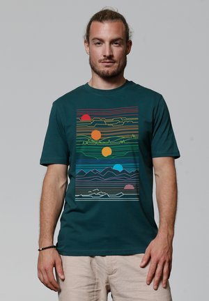 Teal cotton t-shirt featuring a graphic print with multicolored lines, suns in red, orange, and blue, and layered mountain silhouettes.
