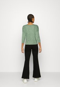 Pulôver verde de mangas compridas com bolinhas brancas, design ajustado e decote arredondado, combinado com calças pretas de boca de sino e sapatilhas brancas.
