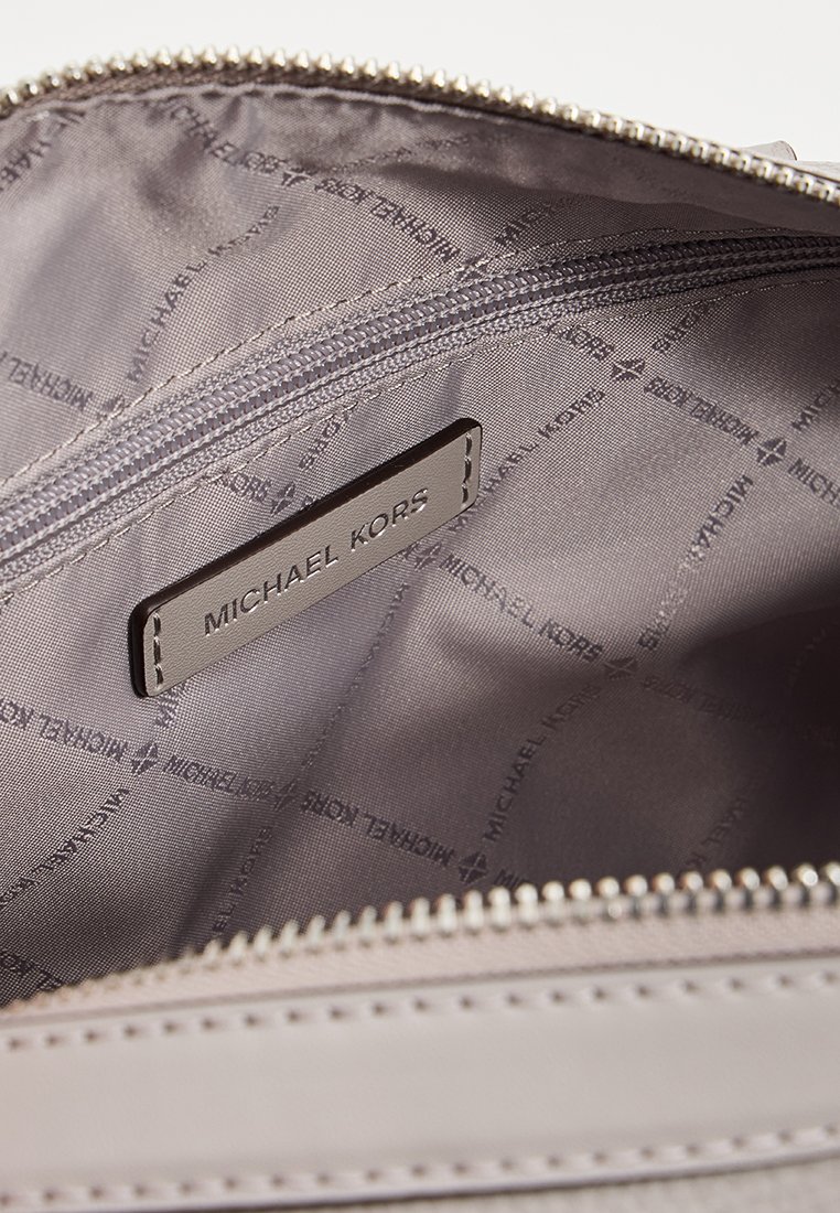 Intérieur gris d'un sac comportant une poche zippée. La doublure présente un motif répété "Michael Kors". Une étiquette de marque en cuir est attachée.