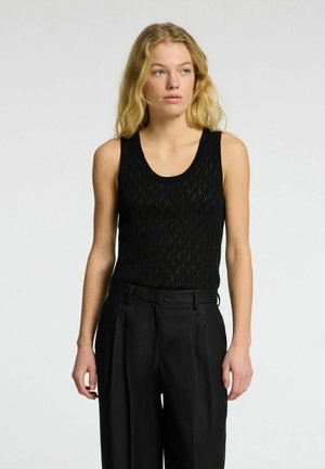 Black knitted tank top with a textured, wavy pattern. Paired with tailored black trousers featuring a high waist and pleated front.