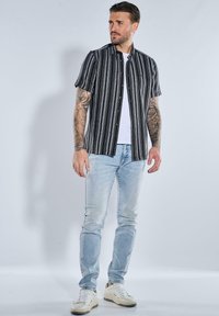 Schwarz-weiß gestreites Kurzarmhemd mit Knöpfen, kombiniert mit hellen Jeans und weißen Sneakers, mit modernem Schnitt und lässigem Stil.