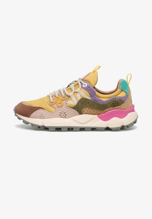 Zapatilla multicolor que presenta una mezcla de gamuza amarilla, marrón, morada y verde. Suela blanca gruesa con acento en rosa y suela texturizada.