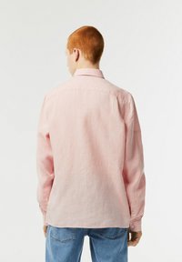 Camisetta a maniche lunghe rosa chiaro realizzata in un tessuto morbido. Presenta un colletto standard, polsini con bottoni e orlo curvo. Design pulito e semplice.