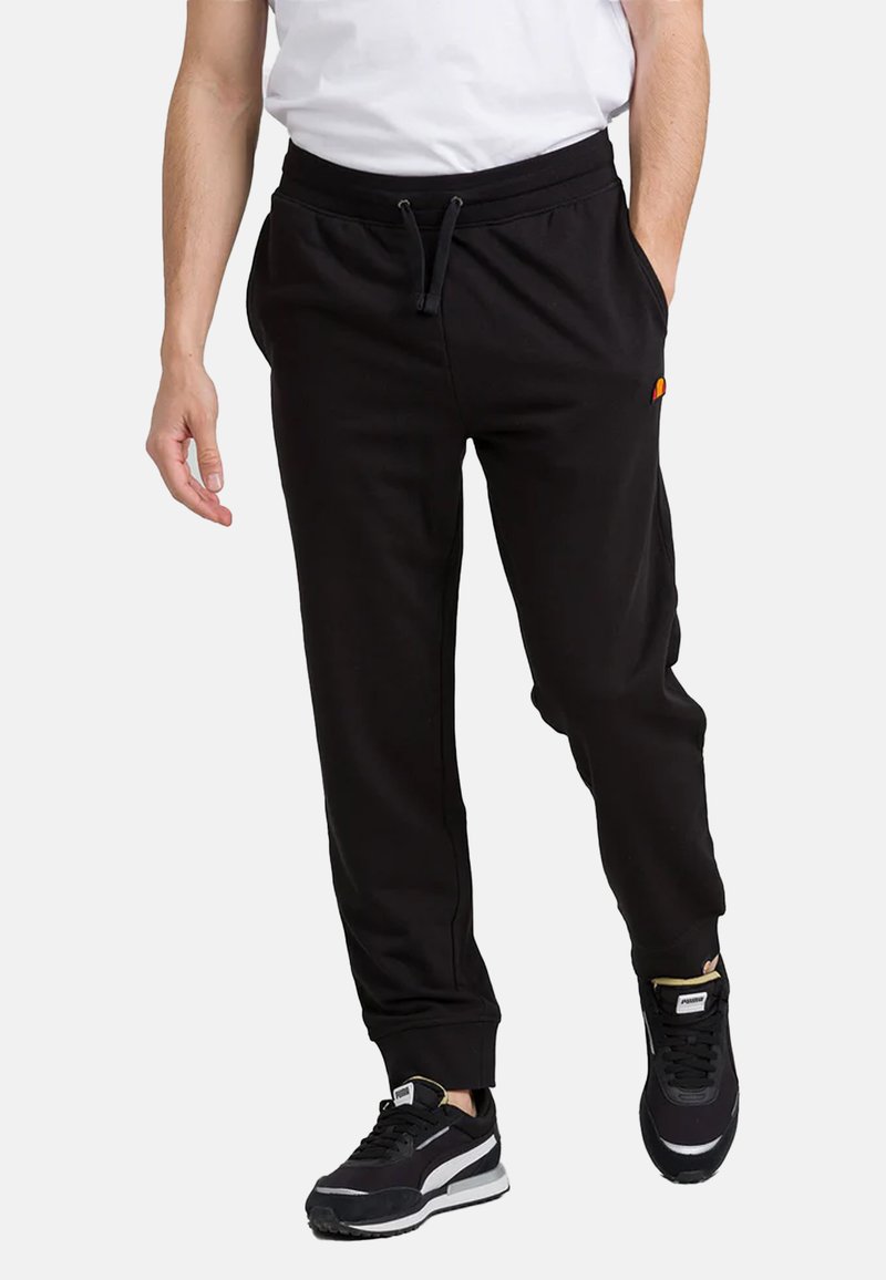 Pantaloni jogger neri con vita elasticizzata e cordino, dotati di tasche laterali e un piccolo logo decorativo. Abbinati a scarpe da atletica nere.