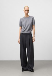 Maglione di lana grigio a maniche corte abbinato a pantaloni scuri a gamba larga. L'insieme presenta una vestibilità comoda e un design minimalista.