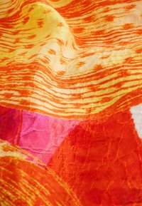 Tissu lumineux avec des rayures ondulées orange et jaune, patch rose et détails de couture texturée visibles.