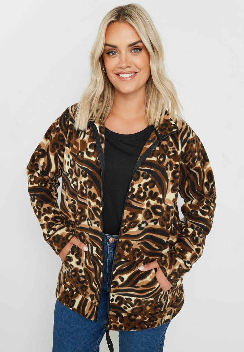 Brun- och svart djurtryck zip-up fleecejacka med framfickor, huva och avslappnad passform, tillsammans med en svart topp och denimjeans.