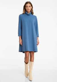 Blaues, locker sitzendes Kleid mit hohem Ausschnitt und Dreiviertelärmeln aus weichem Stoff, mit seitlichen Schlitzen und ausgestelltem Saum.