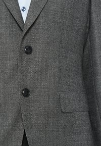 Sivý textured blejzer s dvoma čiernymi gombíkmi, s klopovým golierom a jednou náprsníkovou vreckom. Tkanina je tkána s jemným vzorom.