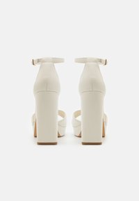 Scarpe con tacco alto bianche, con finitura in pelle liscia, tacco quadrato, cinturino alla caviglia regolabile e design con punta aperta.