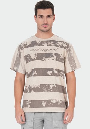 Young man wearing a beige and brown striped t-shirt with distressed texture and the text "mod original" on the chest.