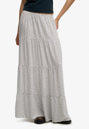 Frau trägt einen mehrlagigen weißen Maxirock mit kleinem blauem Blumenmuster und schwarzen Stiefeln.