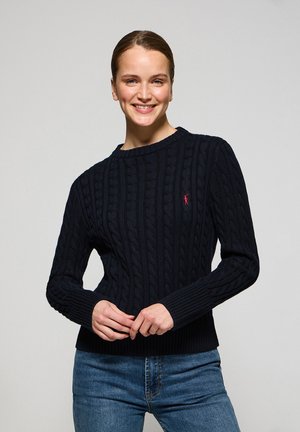 Navy cable-knit sweater with ribbed cuffs and hem; features a small red logo on the chest. Soft texture, classic crew neckline, and fitted style.
