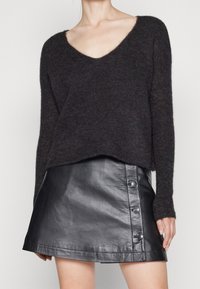 Mörkgrå stickad tröja med vid V-hals och långa ärmar, parat med en svart läder minikjol med knappdetalj på sidan.