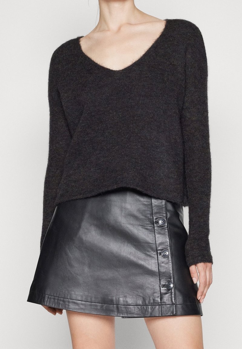 Mörkgrå stickad tröja med vid V-hals och långa ärmar, parat med en svart läder minikjol med knappdetalj på sidan.