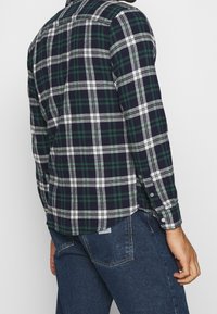 Flanellipaita, jossa on laivastonsininen, vihreä ja valkoinen ruutukuosi. Pitkät hihat, nappimansetit, kaareva helma ja rento istuvuus. Teksturoitu kangas.