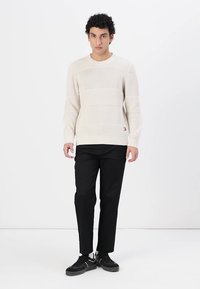 Suéter de punto color crema con rayas horizontales texturizadas, combinado con pantalones ajustados negros y zapatillas negras. Logo notable en el dobladillo.