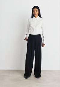 Chemise blanche ajustée avec un col et des manches longues, associée à un pantalon noir à jambes larges taille haute, en tissu lisse, au design minimaliste.