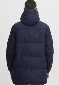Marineblå dunjakke med hette, med quiltet design, elastiske mansjetter og en middels lengde. Glatt, blank tekstur.