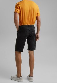 Czarne dżinsowe szorty o prostym kroju, z tylnymi kieszeniami, w połączeniu z pomarańczową koszulką i jasnoszarymi trampkami.