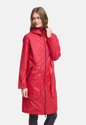 Naine seljas pikk punane kapuutsiga vihmamantel musta tõmbluku ja taskutega, vaadates küljele ühevärvilise heleda tausta ees.