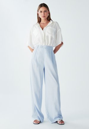 Light blue wide-leg trousers with a high waist and a single button detail, paired with a loose-fitting white shirt featuring two front pockets.
