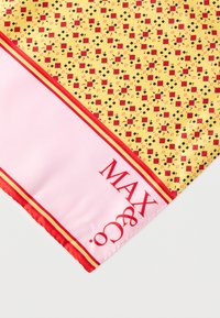 Pañuelo de seda con fondo amarillo y un patrón geométrico en rojo y negro, bordeado por una tela rosa con franjas rojas y marca.