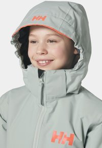 Světle šedá voděodolná bunda s oranžovým akcentem na kapuci a logem. Obsahuje vysoký límec a zipové zapínání.