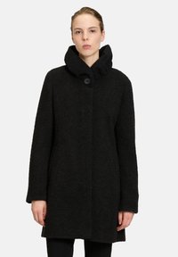 Zwarte wollen jas met een hoge kraag, simpel ontwerp, sluiting met één knoop en textuurstof. Geen zichtbare patronen of accenten.