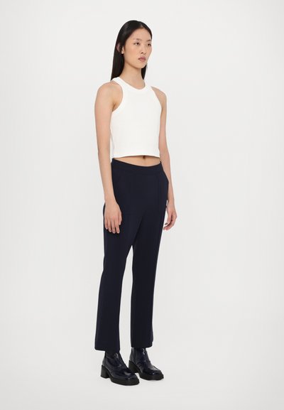 Weißes, kurz geschnittenes Tanktop mit Rundhalsausschnitt, kombiniert mit marineblauen maßgeschneiderten Hosen und schwarzen, glänzenden Leder-Stiefeletten. Geschmeidige Texturen, minimalistisches Design.