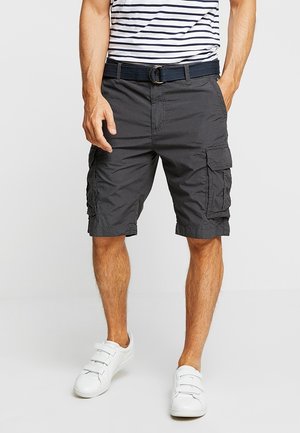Mann trägt schwarze Cargoshorts mit mehreren Taschen, ein gestreiftes Hemd, das hineingesteckt ist, weiße Klettverschluss-Sneaker und einen schwarzen Gürtel.