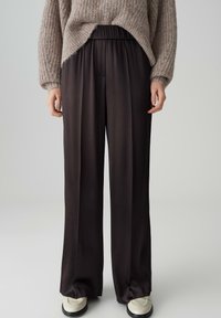 Pantaloni neri a gamba larga con vita elastica, realizzati in un tessuto morbido, caratterizzati da un design pulito e una leggera lucentezza.