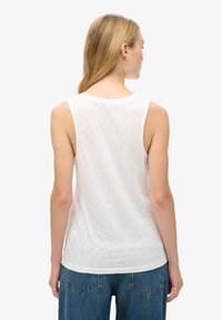 Witte mouwloze top met een ronde halslijn, slim fit en zachte, licht getextureerde stof, gecombineerd met blauwe denim jeans met achterzakken.