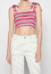 Top corto rojo y blanco con diseño fruncido y tirantes anudados; combinado con jeans de cintura alta, de color claro y ligeramente texturizados.