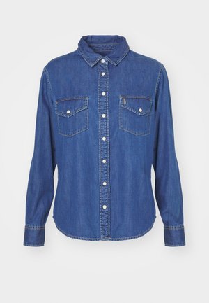 Camisa de denim en azul oscuro, con un cierre de botones al frente, dos bolsillos en el pecho con solapas y un cuello clásico. Manga larga con puños abotonados.