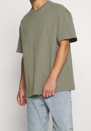 T-shirt en coton vert olive avec une coupe décontractée, manches courtes et col rond, associé à un jean bleu clair.