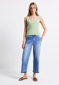 Canottiera verde chiaro, jeans a gamba larga blu con orlo sfrangiato e sandali marroni. Texture liscia, design casual e parte superiore aderente con fit inferiore morbido.