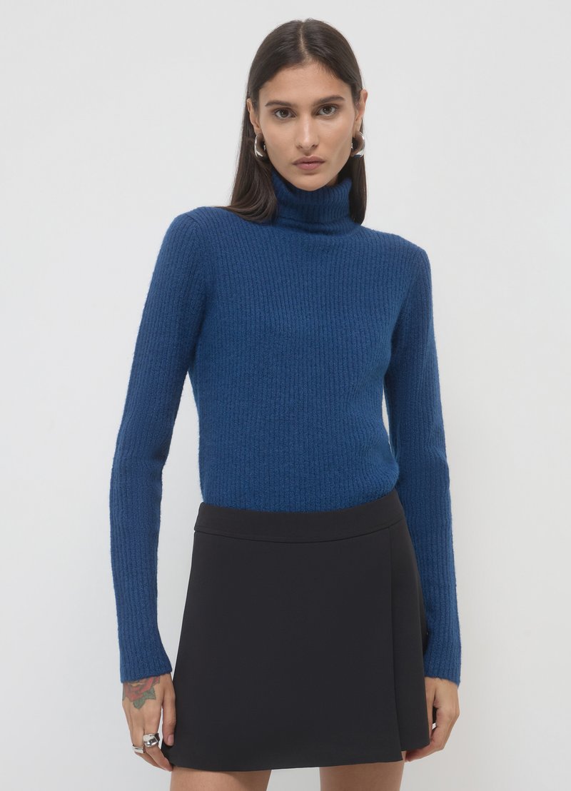 Blue ribbed turtleneck sweater with long sleeves paired with a black skirt, showcasing a fitted design and textured fabric.